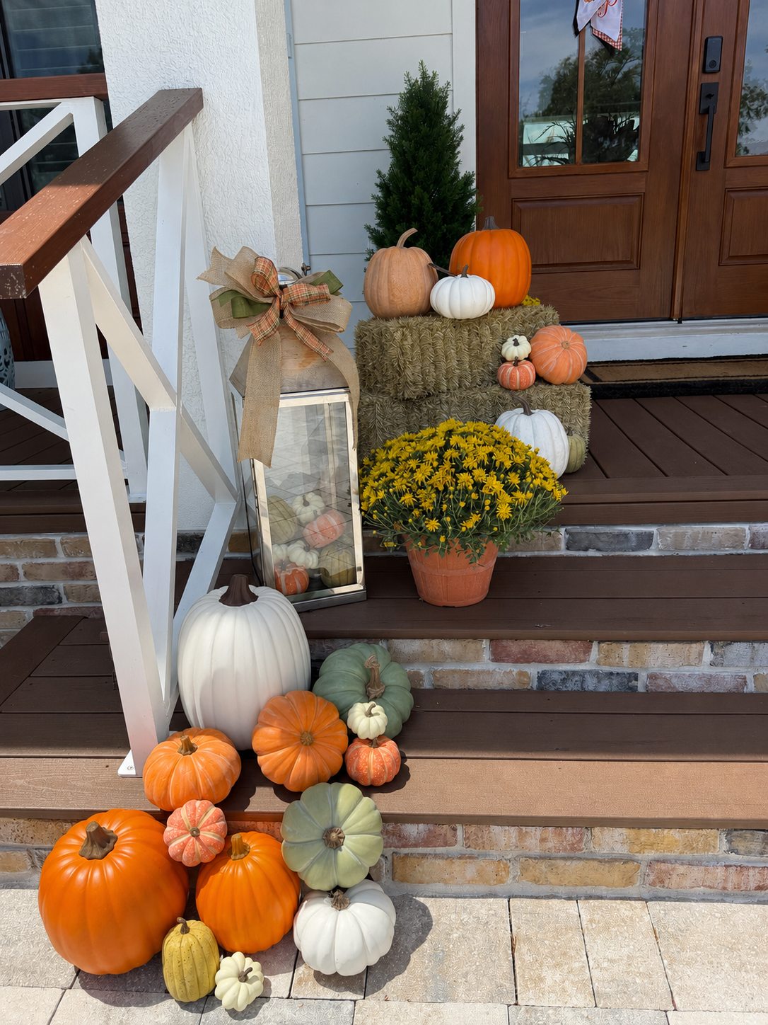 Layered pumpkin, mum and hay bale display on a front porch staircase